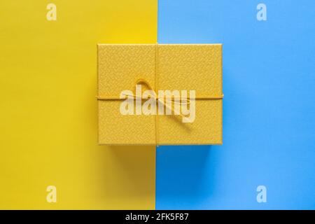 Yellow gift box on blue and yellow background with copy space for text. Holiday greeting or shopping concept Stock Photo