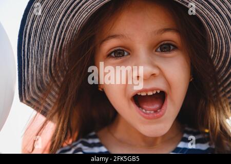 Close up fun portrait of cute laughing little girl in striped sunhat and shirt looking at camera. Selective focus Stock Photo