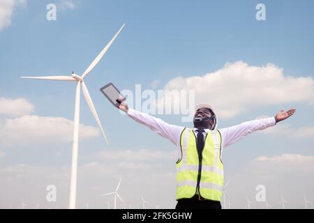 Successful african engineer windmills standing and hoding tablet with wind turbine in background Stock Photo