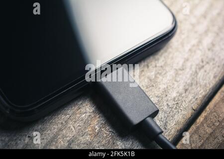Black Smartphone With Connected Black USB Cable On A Wooden Board Stock Photo