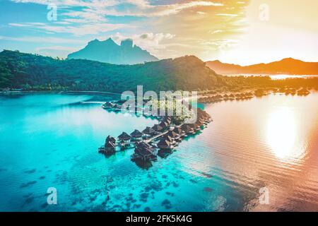 Luxury travel vacation aerial of overwater bungalows resort in coral reef lagoon ocean by beach. View from above at sunset of paradise getaway Bora
