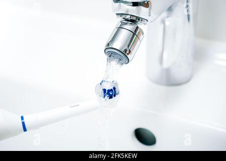 Cleaning An Electric Toothbrush Under Pouring Water At Bathroom Sink