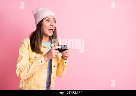Portrait of beautiful young lady playing games gamepad in hands open mouth wear cap isolated on pink color background Stock Photo