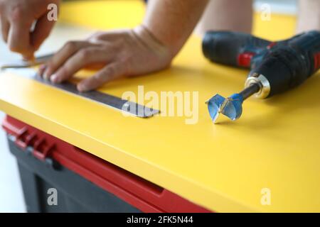 Close-up of drill with nozzle and metal ruler laying on yellow wooden surface Stock Photo