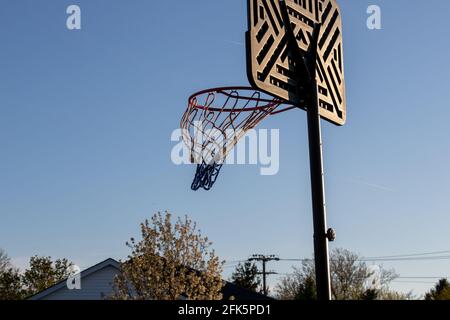 Basketball net on black plastic pole and backboard. Basketball net blowing in wind at sunset. Low angle view against background of blue evening sky. Stock Photo