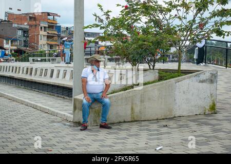 Guatapé, Antioquia, Colombia - April 4 2021: A Latin Man Dressed with a Traditional Hat is Smokes while Sitting in the Plaza Stock Photo