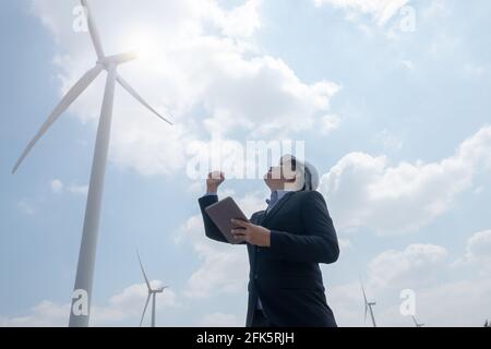 Successful engineer windmills manager standing and hoding tablet with wind turbine in background Stock Photo