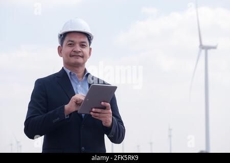 Successful engineer windmills manager standing and hoding tablet with wind turbine in background Stock Photo