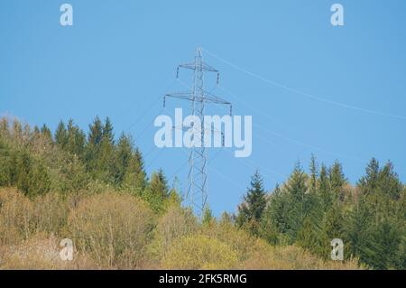 View on a high voltage electric transmission tower on a mountain and against a blue sky in Switzerland Stock Photo
