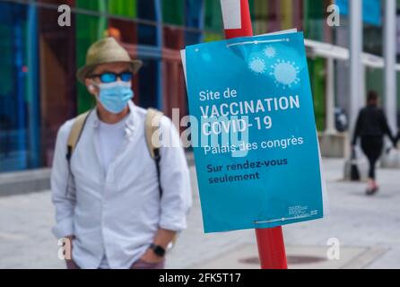 Montreal, CA - 28 April 2021 : Man wearing protective face mask walking next to a Covid-19 vaccination centre sign at Palais des Congres Stock Photo