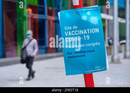 Montreal, CA - 28 April 2021 : Man wearing protective face mask walking next to a Covid-19 vaccination centre sign at Palais des Congres Stock Photo