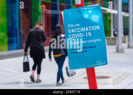 Montreal, CA - 28 April 2021 : Two women walking next to a Covid-19 vaccination centre sign at Palais des Congres Stock Photo