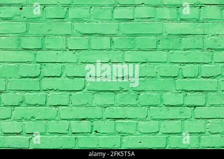The bright texture of an old brick wall is completely painted with green paint in sunlight. A high resolution. Stock Photo