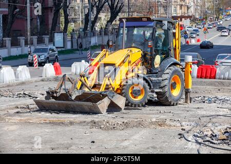 A compact tractor with pavement repair attachments stands on a work platform against the backdrop of a city street. Stock Photo