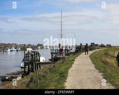 Walker in the distance on the footpath alongside jetties on the River Blyth at Walberswick looking across to boats moored at Southwold Harbour. Stock Photo