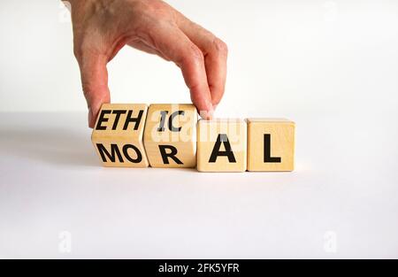 Ethical or moral symbol. Businessman turns wooden cubes and changes the word 'moral' to 'ethical' on a beautiful white table, white background. Busine Stock Photo