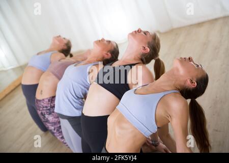 Group of young sporty attractive women in yoga studio, practicing yoga lesson with instructor. Stock Photo