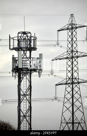 Close up of a silhouetted Cellular network phone mast and electric lattice tower pylon Stock Photo