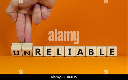 Unreliable or reliable symbol. Businessman turns wooden cubes and changes the word unreliable to reliable. Beautiful orange background, copy space. Bu Stock Photo