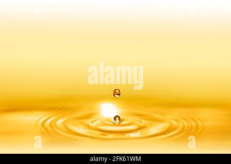 Macro shot of droplets splash of a golden elixir for beauty and body care creating circular waves by falling down on the shining liquid. Stock Photo
