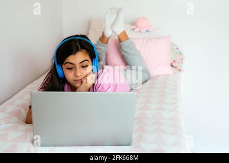 Teen student using laptop and listening to music on bed Stock Photo