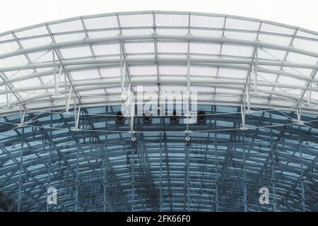 A bluish contemporary glass facade and the roof of a modern building with multiple metal beams and tubes, tiled glass blocks, and four ventilation pip Stock Photo