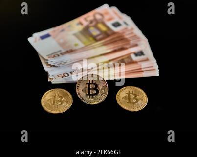 Distant view of a group of Euro banknotes, next to three Bitcoin coins. on a black background. Concept of economy, money, power, elegance, exchange, power, Btc. Selective focus. Stock Photo