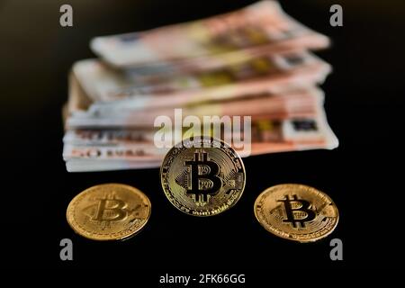 Front view of three Bitcoin coins, next to a group of Euro banknotes, on a black background. Concept of money, power, economics, anonymity, Btc. Selective focus. Stock Photo