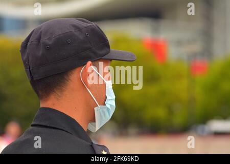 Security guard wearing a correctly fitted medical mask watching people in a Chinese park Stock Photo