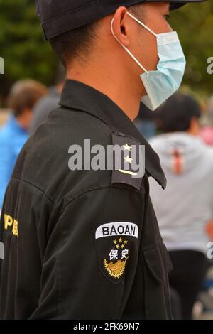 Security guard wearing a correctly fitted medical mask watching people in a Chinese park Stock Photo