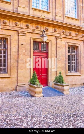 The wall with garlands, vintage lamp, columns and a wooden red door - the side entrance to the City Hall (Hotel de Ville), Aix-en-Provence, France Stock Photo