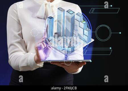 Female real estate agent with tablet computer and digital projection of buildings on dark background Stock Photo
