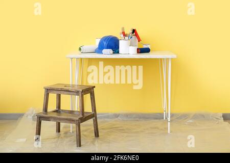 Cans of paints and tools on table near color wall Stock Photo