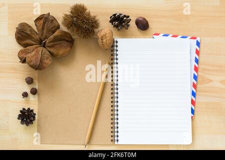 Top view of blank notebook with airmail envelope dried pine cone chestnut walnut cover on wooden background Stock Photo