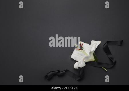 Black funeral ribbon with lily flower on dark background Stock Photo