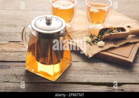 Teapot with hot tea, glasses and dry leaves on wooden background Stock Photo