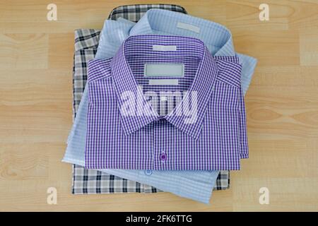 Stack of folded checked clothes, three 3 shirts after ironed ready to pack, on wooden background Stock Photo