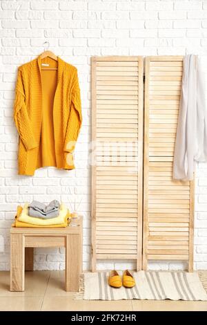Folding screen and table with stylish clothes in modern room Stock Photo
