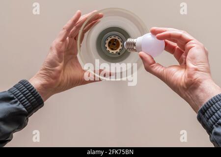 Bottom view of the hands of a man who is changing a light bulb to the chandelier attached to the ceiling of a room Stock Photo