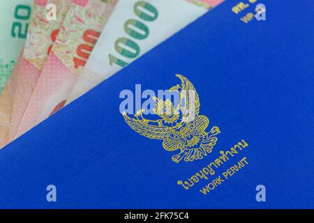 Selective focus of blue Thai Work Permit book (WP.11) on Thai Baht banknote money Stock Photo