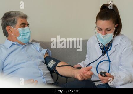Young female doctor checks blood pressure to an old man at home Stock Photo