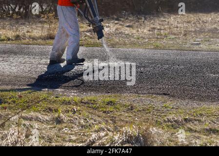 Spring fast repair of an asphalt road. Worker in uniform during fast repair road surface. granite crushed stone and molten tar, bitumen. Stock Photo