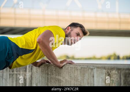 Young man is exercising outdoor. He is doing push-ups. Stock Photo