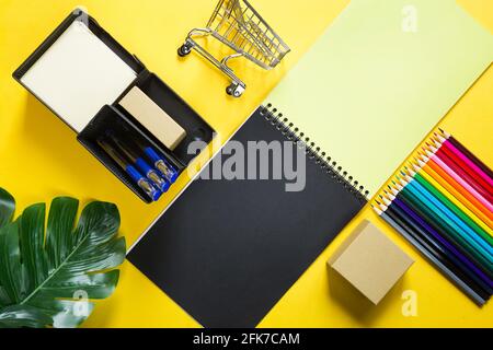 Layout of multi-colored stationery on a yellow background: spiral notebook, colored pencils, stand, pens, indoor flower. Business flat lay, mock up. S Stock Photo