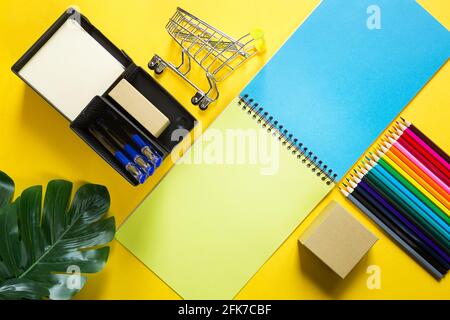 Layout of multi-colored stationery on a yellow background: spiral notebook, colored pencils, stand, pens, indoor flower. Business flat lay, mock up. S Stock Photo