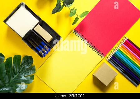 Layout of multi-colored stationery on a yellow background: spiral notebook, colored pencils, stand, pens, indoor flower. Business flat lay, mock up. S Stock Photo