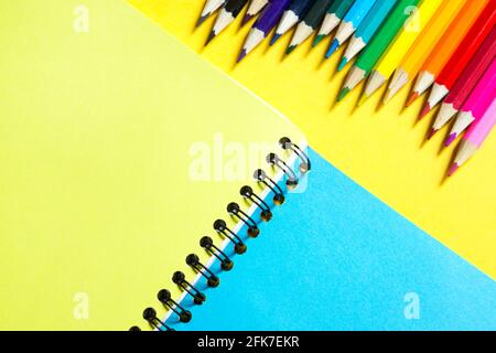 Rainbow palette of colored pencils with a spiral notebook on a yellow background,mock up, flat lay. Back to school, student recruitment, artist, drawi Stock Photo