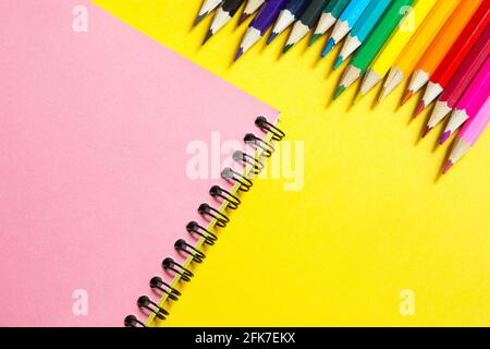 Rainbow palette of colored pencils with a spiral notebook on a yellow background,mock up, flat lay. Back to school, student recruitment, artist, drawi Stock Photo