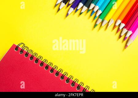 Rainbow palette of colored pencils with a spiral notebook on a yellow background,mock up, flat lay. Back to school, student recruitment, artist, drawi Stock Photo