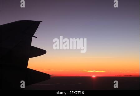 The sun rising over the sea of clouds as seen from plane window Stock Photo